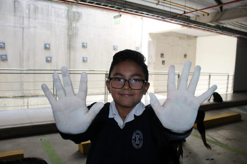 Un niño participante en la intervención artística “Parqueadero” de la Muestra Arte Accesible, extendiendo sus brazos hacia adelante mostrando a la cámara sus manos pintadas con tiza.