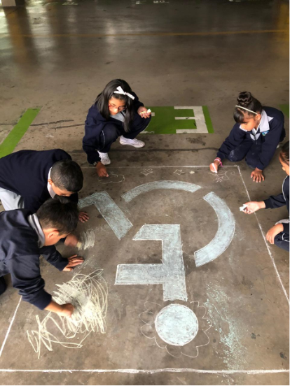 Un grupo de niños realizando una intervención artística en el suelo del Parqueadero de la Asamblea Nacional del Ecuador, acción enmarcada en la Muestra Arte Accesible, llevada a cabo en diciembre de 2019 en Quito, Ecuador.