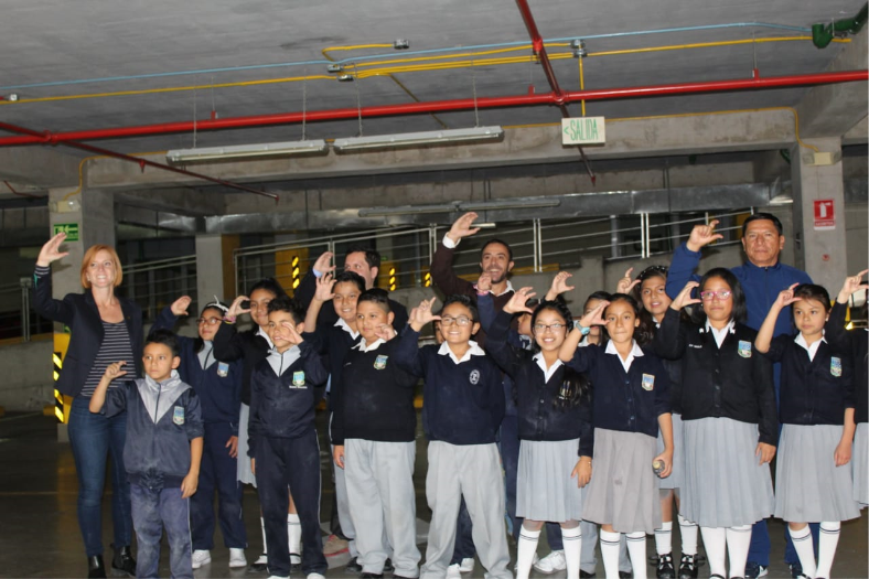 El grupo de alumnos participantes en la intervención artística “Parqueadero” posan para la foto levantando su mano derecha y haciendo la seña de la letra C con sus dedos.