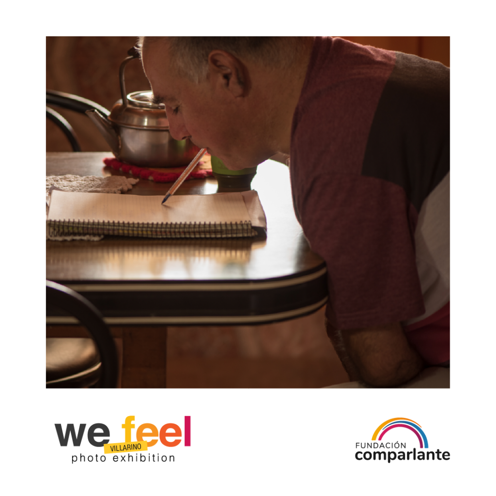 Photo of Horacio, Rights Promotor, writing on a sheet of paper with a pen held with his mouth. Belo, there is the logo of We Feel and Fundación Comparlante.