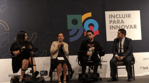Foto de Sebastián Flores sentado conversando con otros 3 panelistas en el escenario. Detrás de ellos hay una logo y un texto que titula. “Incluir para innovar”