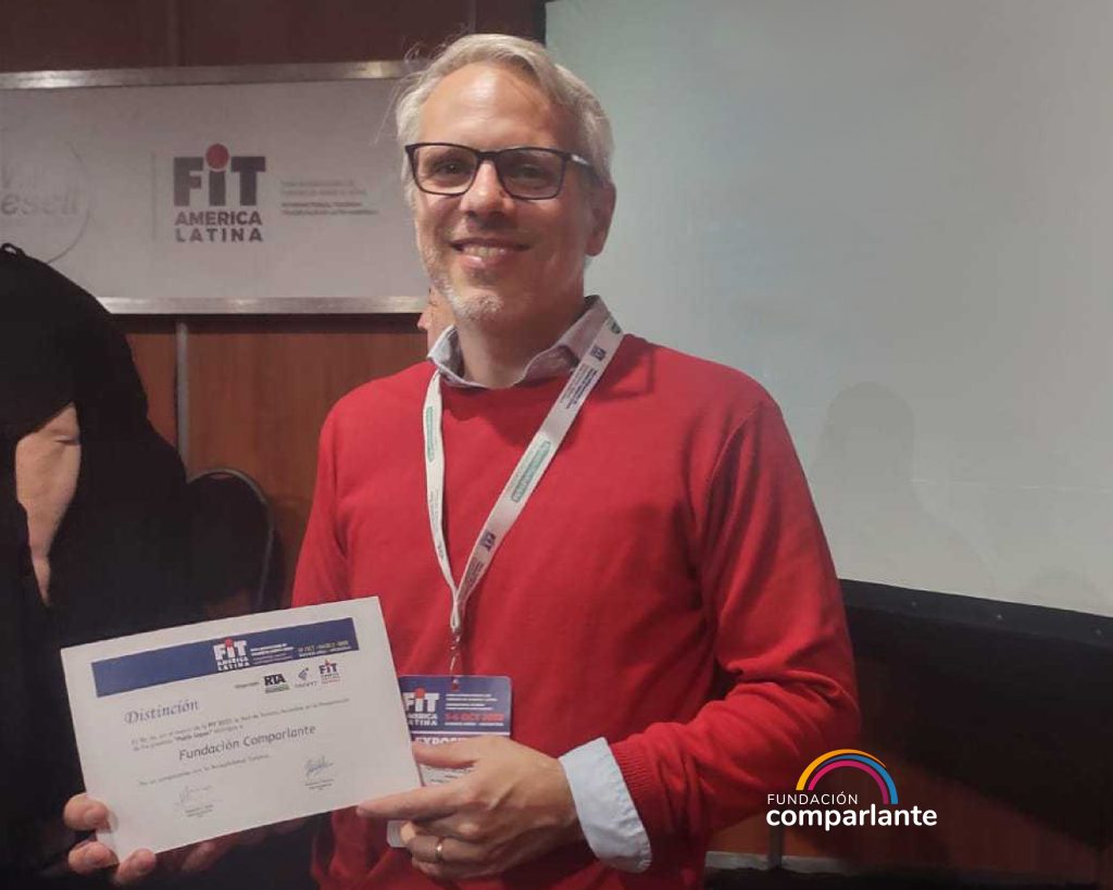 Photo of Lautaro Mallo, a member of Fundación Comparlante, smiling to a camera whilst he is holding the certificate of merit. He is at Villa Gesel auditorium at the event International Tourism Fair in Latin America.