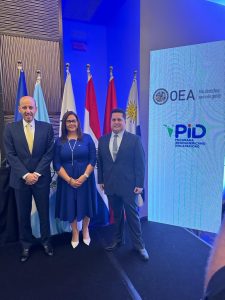 Sebastián next to the General Director of the National Secretariat for Persons with Disabilities, Iris González de Valenzuela, and Rubén Farje, OAS representative in Panamá. They smile at the camera next to the OAS banners for the Inter-American Program on Disability and the flags of the States.