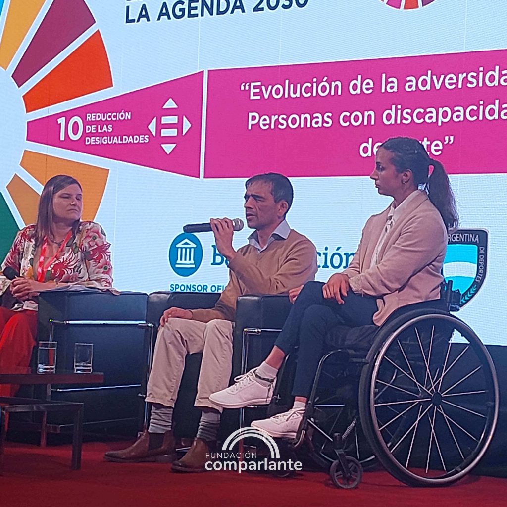 Fotografia donde Lelio se encuentra sentado en un sillón en el escenario de la Jornada, junto a Brenda Sardon y otra de las presentadora del evento. Lelio sostiene el micrófono en su mano y habla al público.