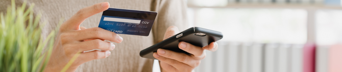 Fotografía de una persona utilizando su tarjeta de crédito y sosteniendo su teléfono celular.