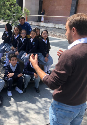 Andrés Julio, artist in charge of the Accessible Art exhibition speaking to a group of students on the grounds of the National Assembly of Ecuador. 6- In the grounds of the National Assembly, a group of Parliamentarians are standing, to one side a Sign Language interpreter appears interpreting the event.